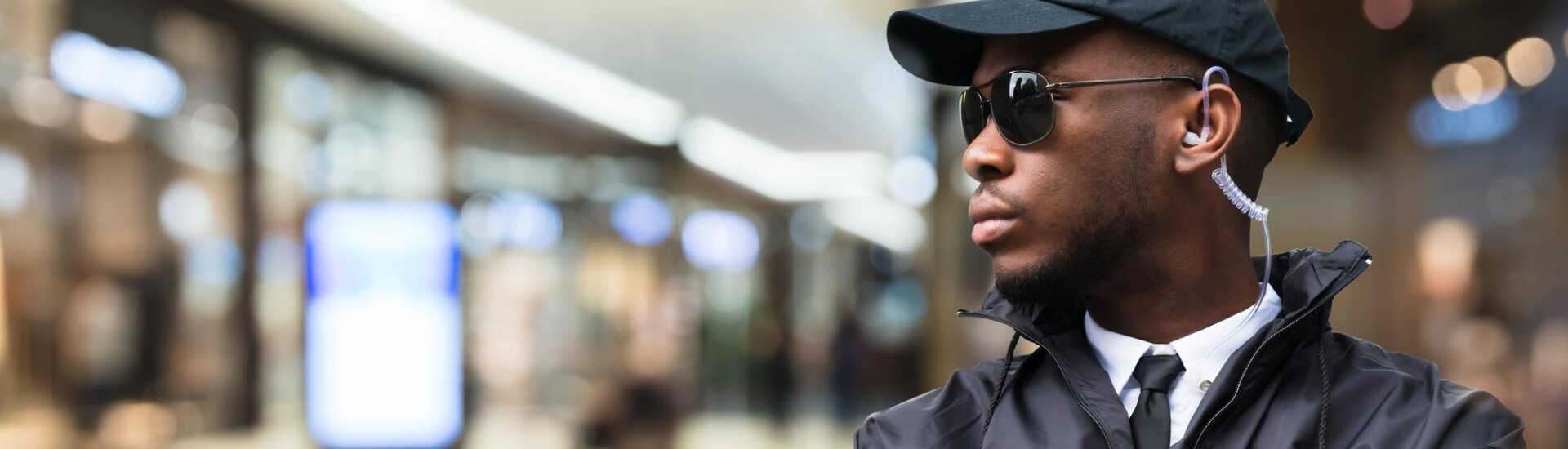 security guard in windbreaker wearing a baseball cap and sunglasses